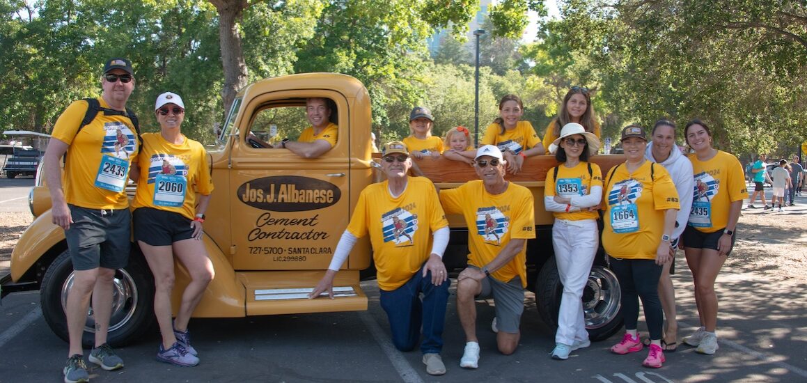 Group of people representing a company sponsoring Summer Scamper pose by a pickup truck with the company name on it.