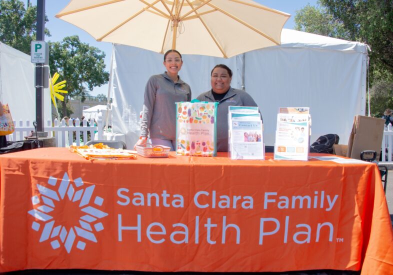 Two women standing behind a Santa Clara Family Health Plan table at Summer Scamper.