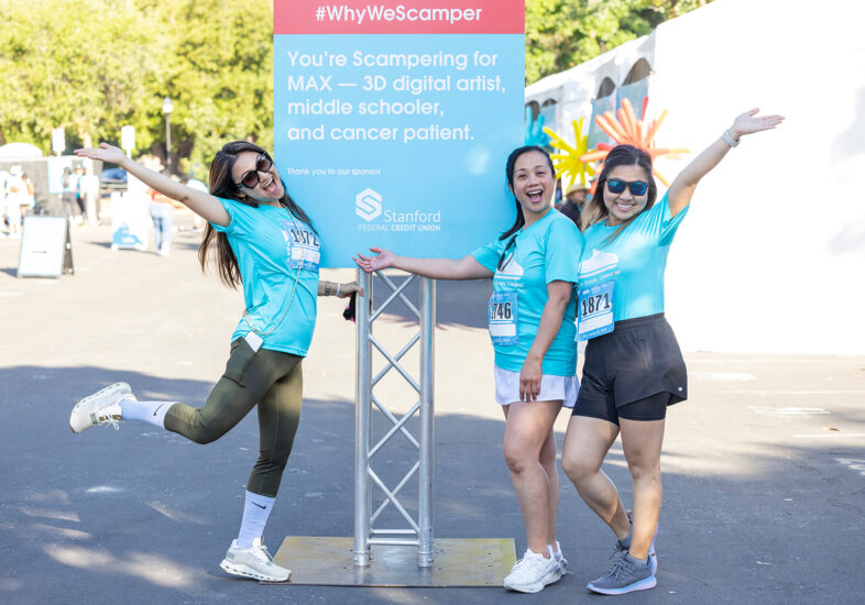 Three women in Summer Scamper shirts pose by a Summer Scamper sign on raceday