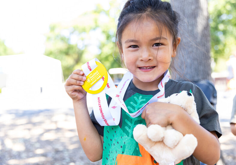 A young girl holds up her participation medal after the kids fun run